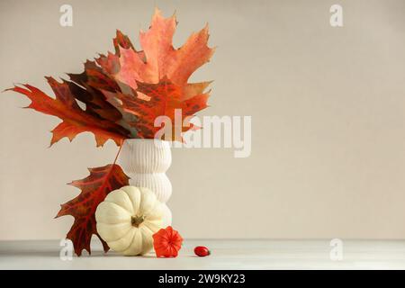 Schöne Herbstblätter in Vase, Kürbis und Physalis auf dem Tisch vor beigefarbenem Hintergrund, Platz für Text Stockfoto