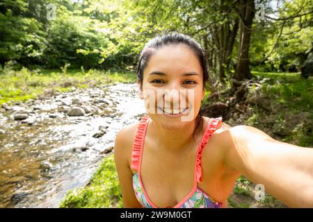 Junge Erwachsene Frau, die ein lächelndes Selfie in einem Fluss in Córdoba, Argentinien macht. Sie ist eine Touristin in einem bunten Bikini. Stockfoto