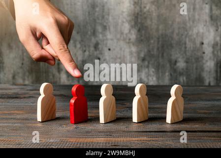 Eine menschliche Hand, die auf eine Holzfigur aus der Reihe der Holzfiguren auf einem Holztisch zeigt Stockfoto