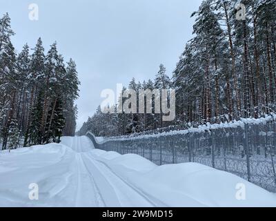 Silene, Lettland. Dezember 2023. Die Straße am Grenzzaun an der Lettisch-belarussischen Grenze ist mit tiefem Schnee bedeckt. Lettland hat eine etwa 172 Kilometer lange Grenze zu Russlands engstem Verbündeten Belarus, das Teil der EU-Außengrenze ist. (An dpa "Lettland: Zaun an der Grenze zu Belarus nähert sich der Fertigstellung") Credit: Alexander Welscher/dpa/Alamy Live News Stockfoto