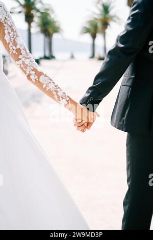 Braut und Bräutigam gehen Hand an der Promenade entlang. Abgeschnitten. Gesichtslos. Rückansicht Stockfoto