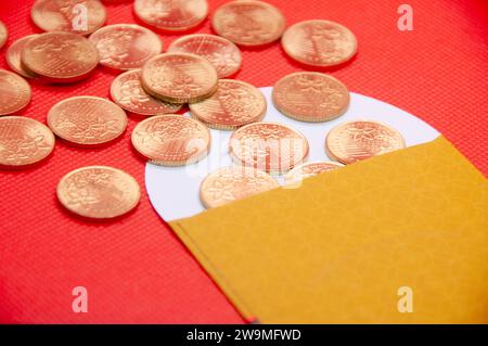 Nahaufnahme des gelben Umschlags und der goldenen Münzen auf rotem Umschlaghintergrund. Stockfoto