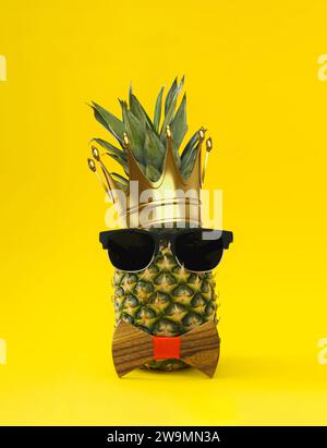 Der König aller Früchte. Kreatives tropisches Sommerlayout aus Ananas mit Krone, Sonnenbrille und Fliege auf hellgelbem Hintergrund. Stockfoto