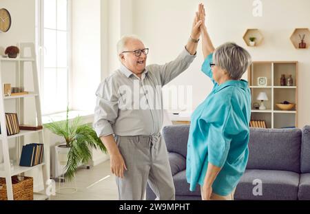Seniorenpaar, das zu Hause steht und sich gegenseitig High Five gibt, um Erfolg zu feiern Stockfoto