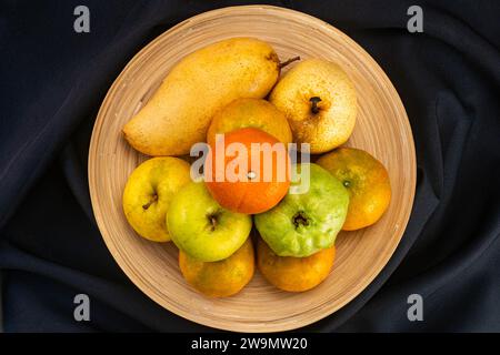 Mit Blick von oben auf verschiedene reife süße tropische Früchte in Bambusschale isoliert auf schwarzem Tuch mit Schneidepfad. Stockfoto