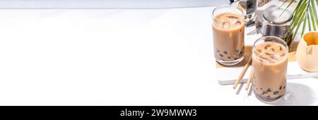 Iced Tapica Coffee Latte oder boba Pearl Bubbles Milchtee, asiatisches trendiges kaltes Kaffeegetränk mit Tapiokasseln und zerstoßenem Eis, auf weißem Marmorhintergrund Stockfoto