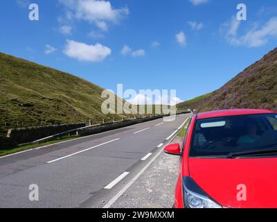 Unerkennbare Frau, die in einem roten Auto sitzt, das am Straßenrand zwischen den Hügeln Snake Road oder Snake Pass im Peak District National Park, Großbritannien, geparkt ist. Stockfoto