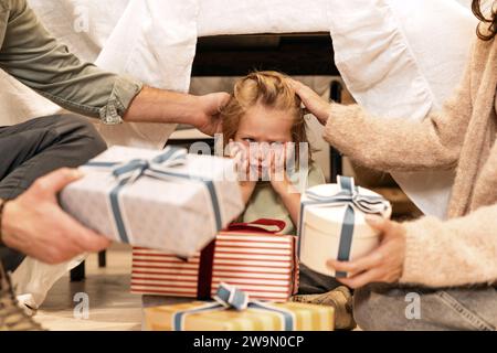 Zwei Eltern, die auf dem Boden sitzen und ihrem unglücklichen Sohn Geschenke schenken Stockfoto