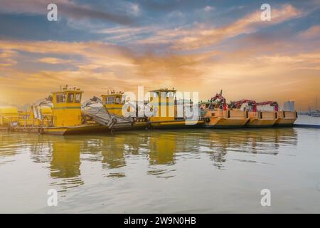 Kleine mehrere Reihen Schiffe mit einem Greifmanipulator, der am Hafenpier am Sonnenuntergang von Hand geparkt ist. Stockfoto