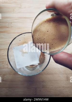 Blick von oben auf eine Person, die einen Espresso über einen Eiswürfel gießt, um einen Eiskaffee zuzubereiten Stockfoto