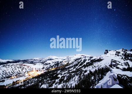 Ein Nachtblick auf das Kirkwood Mountain Resort mit Sternen und der Milchstraße über dem Dach und den Lichtern des Dorfes, die den Talboden in Kirkwood, Kalifornien, erleuchten. Stockfoto