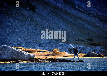 Ein Mann schwingt seine Fliegenrute zurück, fängt Sonnenlicht darauf ein und fischt in der Nähe des Saddlebag Lake in den östlichen Sierra Mountains Kaliforniens. Stockfoto