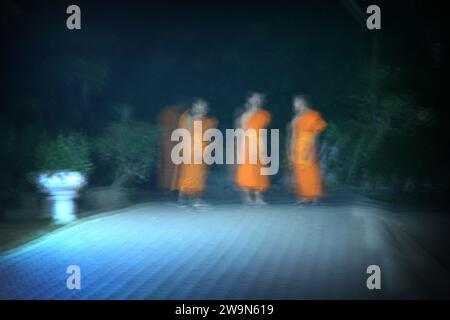 Drei buddhistische Mönche stehen nachts in einem Innenhof, nur von einer Straßenlampe beleuchtet. Chiang Rai, Thailand. (Verschwommene Bewegung) Stockfoto