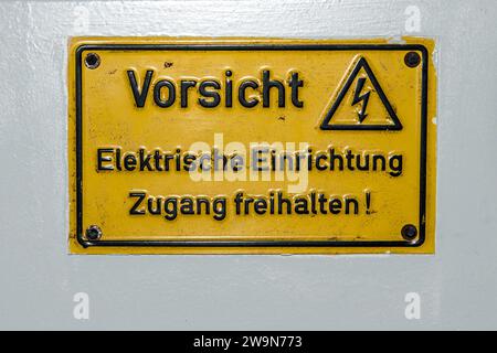 Hochspannungswarnung auf Deutsch mit dem Hinweis, dass das elektrische Gerät auf dem elektrischen Schaltkasten nicht abgedeckt ist. Stockfoto