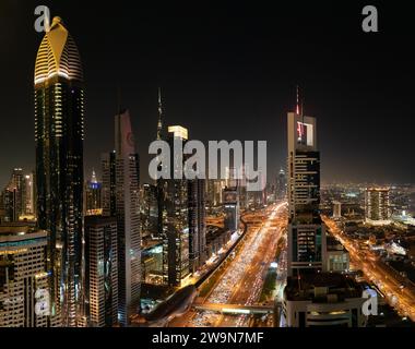 Hoher Aussichtspunkt auf die Sheikh Zayed Road in der Hauptverkehrszeit, Dubai, bei Nacht mit Burj Khalifa in der Ferne und modernen Wolkenkratzern im Vordergrund Stockfoto