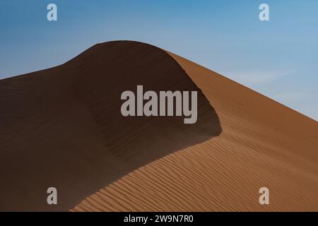 Wind, der über die Spitze einer Sanddüne weht, Morgenlicht. Stockfoto