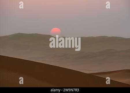 Sonnenaufgang über den Sanddünen mit einer leeren Straße am Horizont, trübem Himmel. Stockfoto