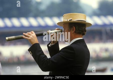 Henley Royal Rowing Regatta. Ein Mann in einem Strohboot-Hut, der das Rennen durch ein Teleskop beobachtet. Henley on Thames, Oxfordshire, England Juli 1985 1980, Großbritannien HOMER SYKES Stockfoto