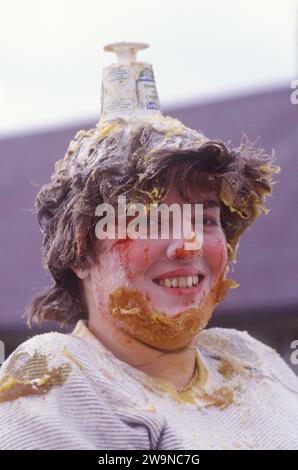 Die Braut und den Bräutigam schwärzen. Ein Folklore-Ritual vor der Hochzeit in Schottland. Ein junges Paar wird durch die Stadt gefahren und sitzt in einer Badewanne auf der Rückseite eines Lastwagens. Sie sind mit Mehl und Eiern bedeckt. Dieses Ritual vor der Hochzeit findet am Tag vor ihrer Hochzeit statt und wird als „Schwärzung“ oder „reschtach“ bezeichnet und schreckt anscheinend böse Geister vor der Hochzeit ab. Mallaig, Schottland 1980er Jahre 1987 Vereinigtes Königreich HOMER SYKES Stockfoto