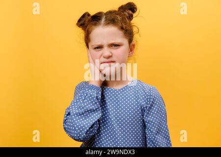 Porträt eines unglücklichen jungen Mädchens, das an Ohrenschmerzen leidet, isoliert über der gelben Hintergrundwand im Studio posiert. Die Ursache für Ohrenschmerzen ist auch Stockfoto