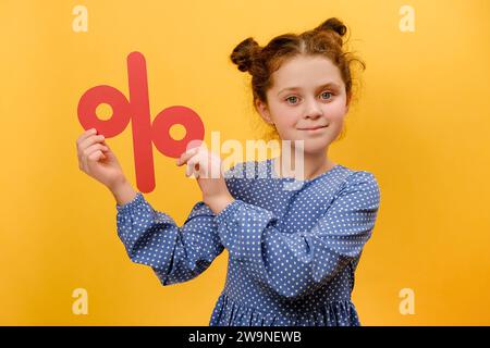 Porträt eines fröhlichen Mädchens mit roter Prozentmarke, das positive Emotionen ausdrückt, Rabatte präsentiert, sich isoliert über Yello posiert Stockfoto