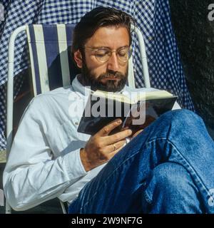 Ein Mann liest ein Buch. Der bärtige Mann sitzt auf einem Stuhl und liest ein Buch. Stockfoto