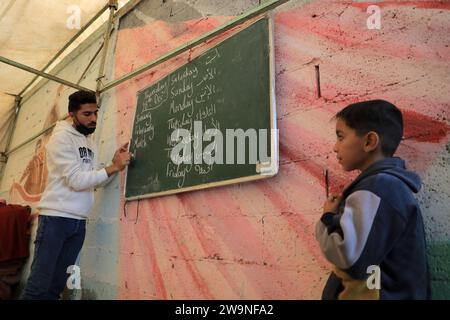 Rafah. Dezember 2023. Ein Lehrer (L) unterrichtet Schüler in einem temporären Klassenzimmer in Rafah im südlichen Gazastreifen am 28. Dezember 2023. Einige Schüler in Gaza haben in vorübergehende Klassenzimmer umgestiegen, da viele Schulen hier für die Unterbringung von Obdachlosen genutzt werden, die durch eine neue Runde des palästinensisch-israelischen Konflikts verursacht wurden. Quelle: Rizek Abdeljawad/Xinhua/Alamy Live News Stockfoto