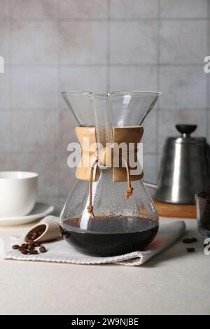 chemex-Glaskaffeemaschine mit leckerem Tropfkaffee und Bohnen auf weißem Tisch Stockfoto