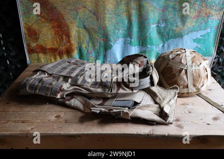 Ein Militärhelm eines ukrainischen Soldaten mit einer schweren kugelsicheren Weste auf einem Holztisch im Innenraum des Kontrollpunktes Stockfoto