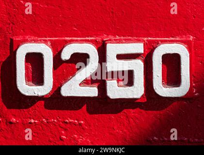 Verwitterte Zahlen Null, zwei, fünf, 0250 oder 0, 2, 5 weiß auf ein Stück rotes Metall gemalt. Numerischer Hintergrund für Design. Stockfoto