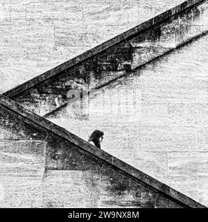 Schwarzweißbild einer Frau, die eine massive, eckige Außentreppe mit rauen und granularen Wänden absteigt. Stockfoto