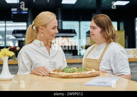 Eine junge Kellnerin mit psychischen Störungen serviert köstliche Pizza in der Nähe einer lächelnden Frau in einem modernen Café Stockfoto