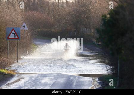 Ein Motorradfahrer, der auf der Newton Lane, Fairburn, North Yorkshire, Großbritannien, durch das Hochwasser gefahren ist Stockfoto