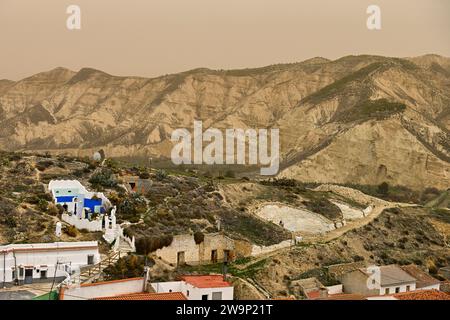 Höhlenhäuser mit unverwechselbaren blauen Türen in einer zerklüfteten Wüstenberglandschaft. Stockfoto