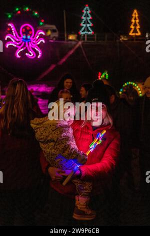 Eine Mutter und ein Kind genießen die Hafenbeleuchtung, eine jährliche Ausstellung von Weihnachtslichtern im kleinen Küstendorf Mousehole, Cornwall, Großbritannien Stockfoto