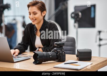 Konzentrieren Sie sich auf die moderne Kamera auf dem Tisch neben einer fröhlichen professionellen Fotografin im Studio Stockfoto