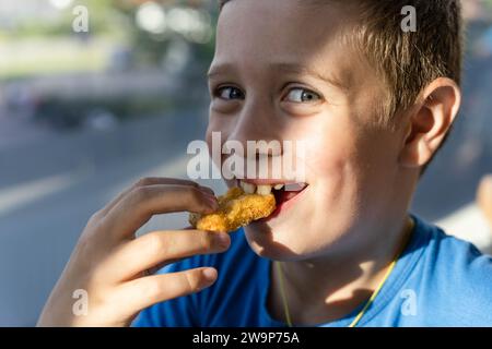 Ein Junge mit einem angenehmen Lächeln genießt köstliche Nuggets, die unbeschwertes Glück und einfache Freuden der Kindheit ausstrahlen. Stockfoto