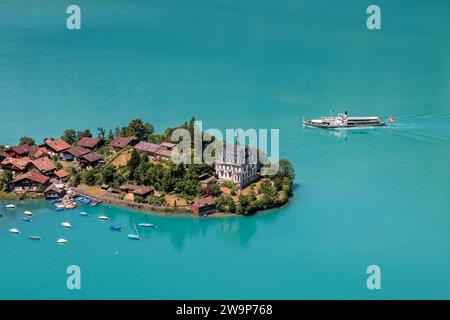 Inseltwakd, Schweiz - 18. Juni 2022: Blick über das Dorf Iseltwald am türkisfarbenen Brienzersee mit einem Ausflugsschiff auf dem See, Schweiz Stockfoto
