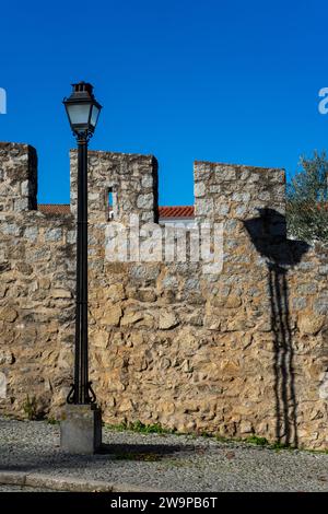 Die traditionelle Straßenlaterne wirft Schatten auf die historische Wand von Evora. Stockfoto