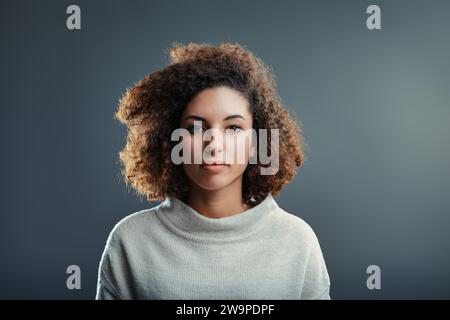 Die sanften Augen und die entspannten Locken der jungen Frau drücken Ruhe vor dem neutralen Hintergrund aus Stockfoto