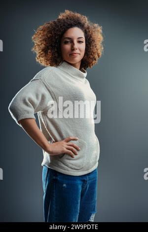 Introspektive junge Frau mit natürlichen Locken zeigt eine kontemplative Stimmung, ihre Kleidung ist untertrieben Stockfoto