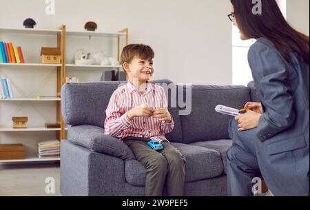 Junge Psychologin, die sich mit einem lächelnden kleinen Jungen während des Treffens unterhalten hat Stockfoto