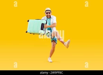 Ein überfröhlicher junger Mann mit Koffer geht in Sommerferien auf gelbem Hintergrund. Stockfoto