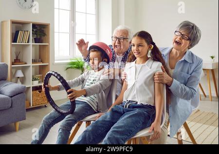 Glückliche Großeltern und Kinder, die zu Hause spielen, vorgeben, Auto zu fahren und Spaß zu haben Stockfoto