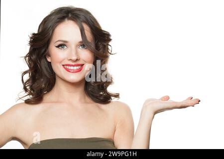 Schöne junge glückliche Frau, die leere offene Hand für Werbemarketing oder Produktplatzierung zeigt. Schönes Modemodell mit Make-up und langem Blond Stockfoto