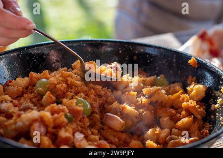 Beim Kochen des typischen spanischen Gerichts „Migas Castellanas“ über einem Holzfeuer können Sie den gesamten Prozess mit seinen Zutaten wie Brot, Stockfoto