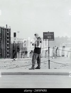 Mann liest eine Zeitung neben dem Schild mit der Aufschrift "U.S. Property, no Trespassing", Battery, New York City, New York, USA, Angelo Rizzuto, Anthony Angel Collection, Mai 1952 Stockfoto