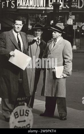 Drei Geschäftsleute in Mänteln reden auf dem Bürgersteig, zwei halten Zeitungen, während der Mann in der Mitte mit dem Finger zeigt, West 43rd Street, New York City, New York, USA, Angelo Rizzuto, Anthony Angel Collection, November 1953 Stockfoto