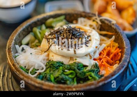 Koreanischer vegetarischer Bibimbap, gebratener Tofu und Gemüse in einer heißen Steinschale. Stockfoto