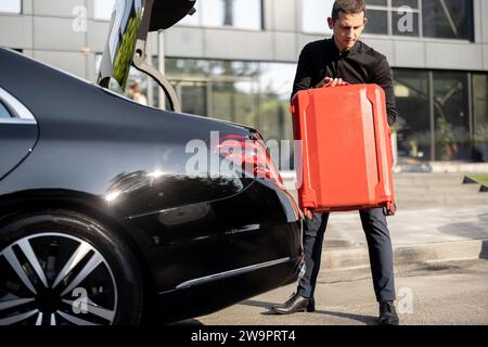 Chauffeur packt einen Koffer in ein Luxusauto Stockfoto